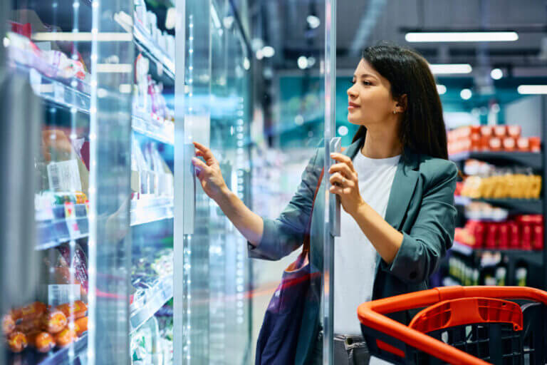 Consumidora abre una góndola refrigerada en un supermercado, donde las góndolas conectadas ayudan a reducir faltantes y errores de precio.