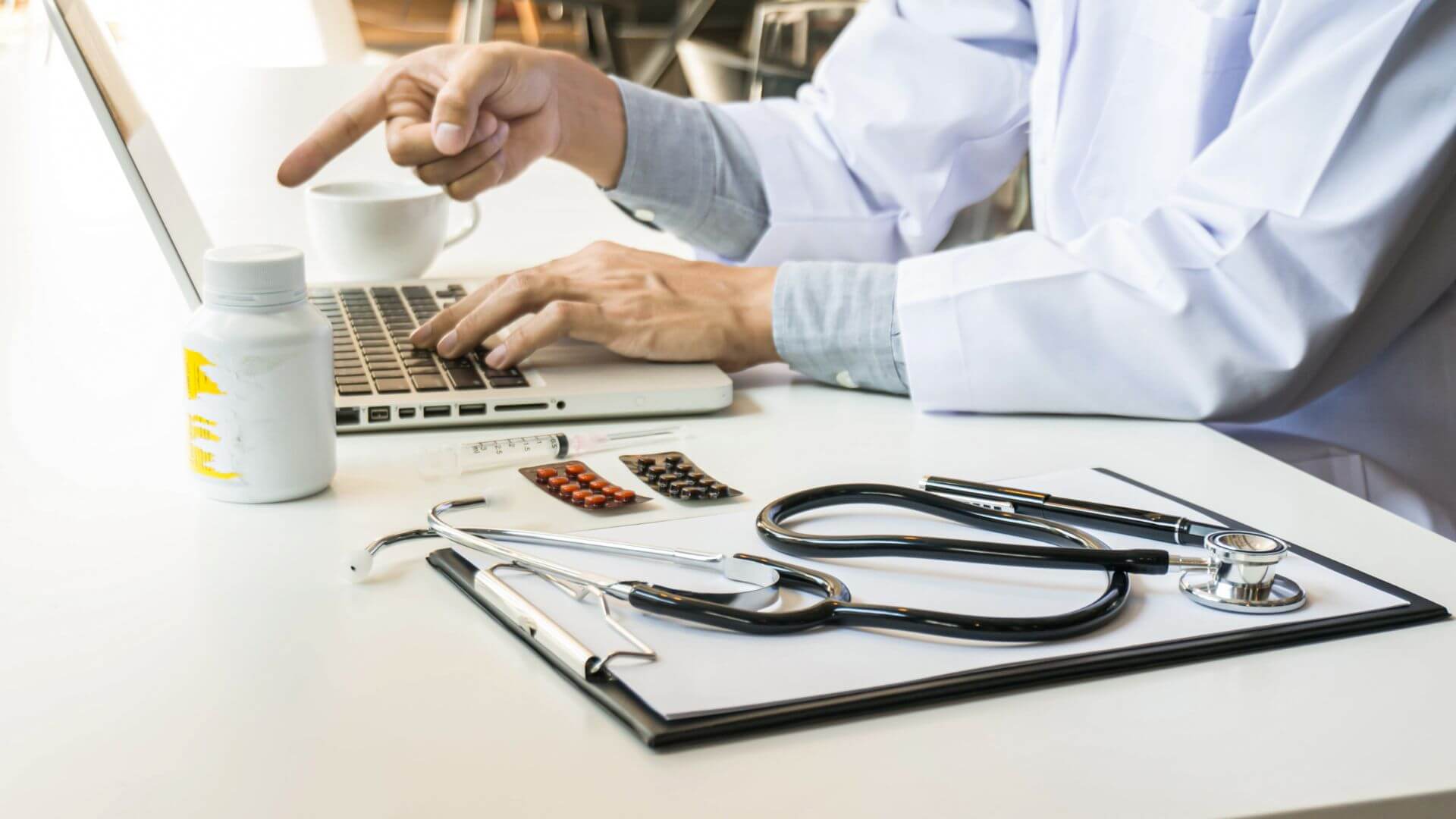 Profesional de la salud trabaja con una notebook junto a medicamentos y un estetoscopio, en un entorno asociado a hospitales inteligentes.