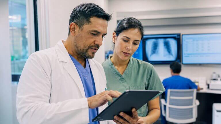 Médico y profesional de enfermería consultan información en una tablet dentro de un hospital inteligente.