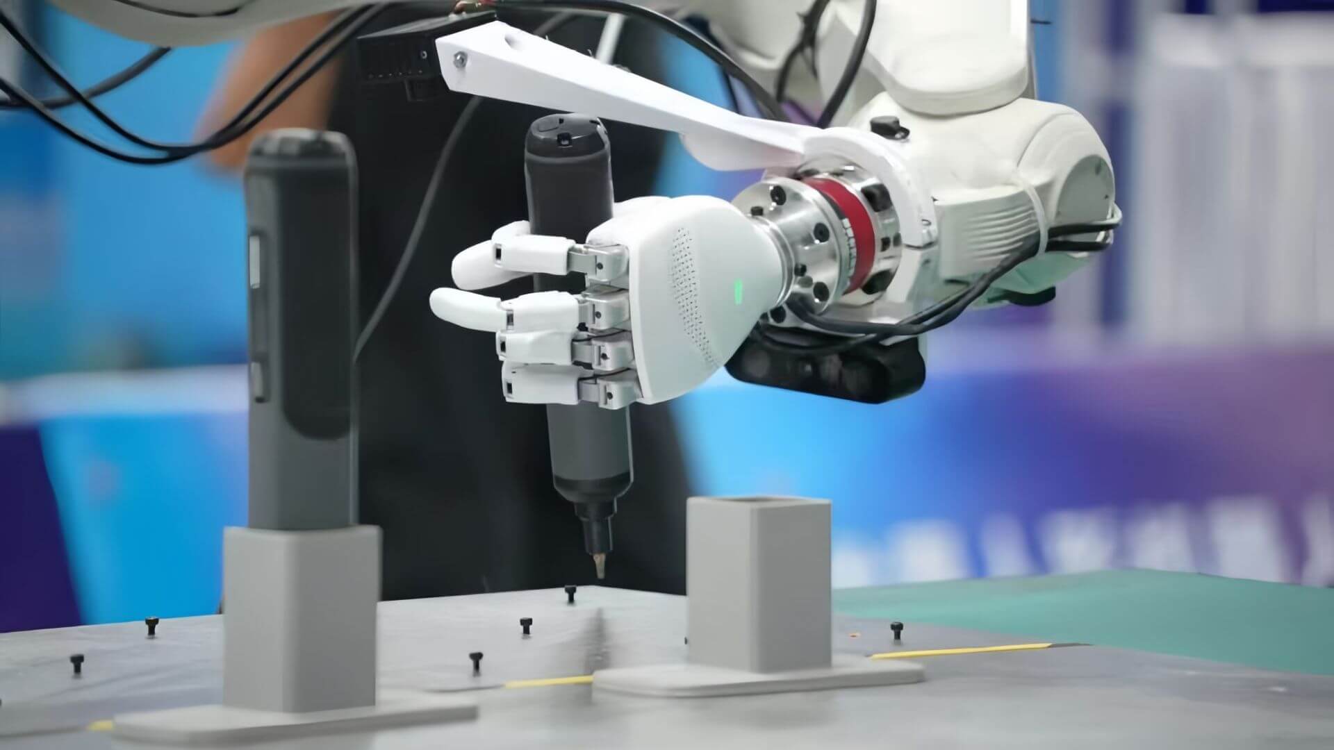 Mano robótica de Linkerbot montada en un brazo mecánico que manipula una herramienta sobre una mesa con tornillos.