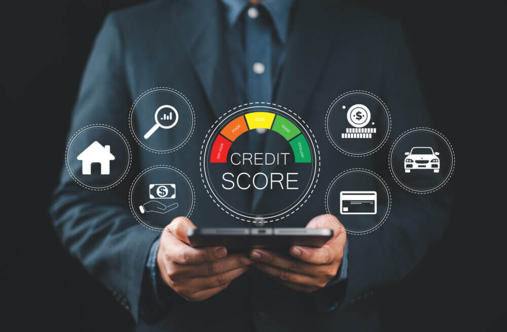 Persona sostiene una tablet frente a un indicador digital de scoring crediticio con íconos de vivienda, dinero, tarjeta y vehículo.
