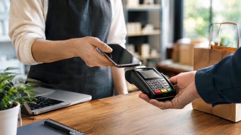 Persona realizando un pago con celular mediante una terminal de cobro en un pequeño comercio.