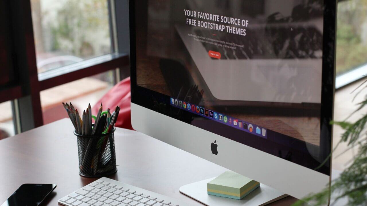Computadora de escritorio Apple iMac sobre un escritorio, junto a un teclado, un teléfono y elementos de oficina.