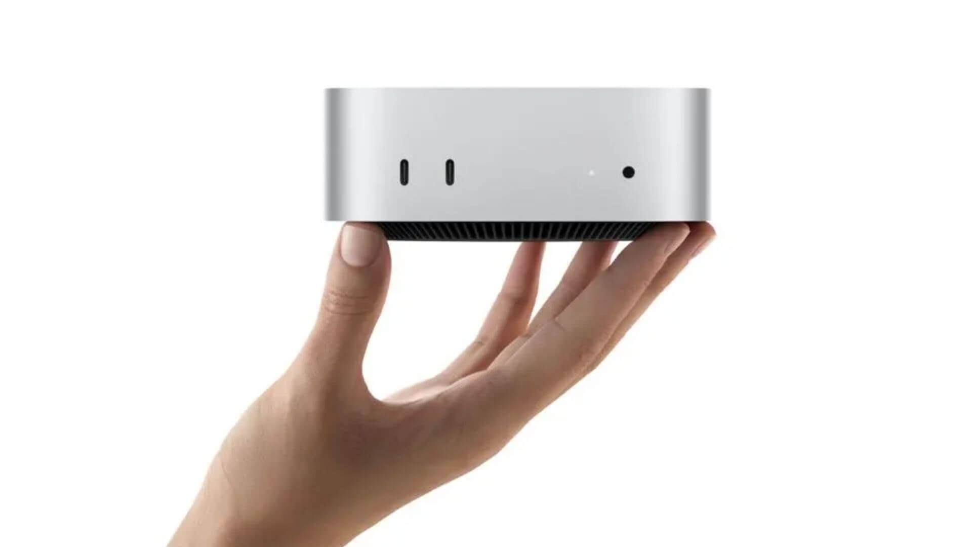 Apple Mac mini plateada sostenida sobre una mano, con sus puertos frontales visibles sobre fondo blanco.