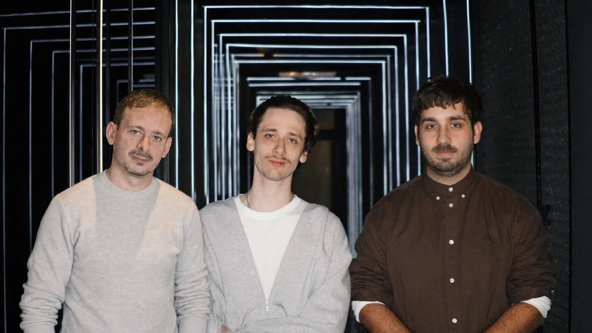 Tres integrantes del equipo de Endless posan frente a una estructura iluminada, en una imagen institucional de la compañía tecnológica.