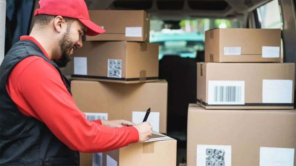 Repartidor de courier anota datos en una caja junto a otros paquetes en una camioneta de reparto.