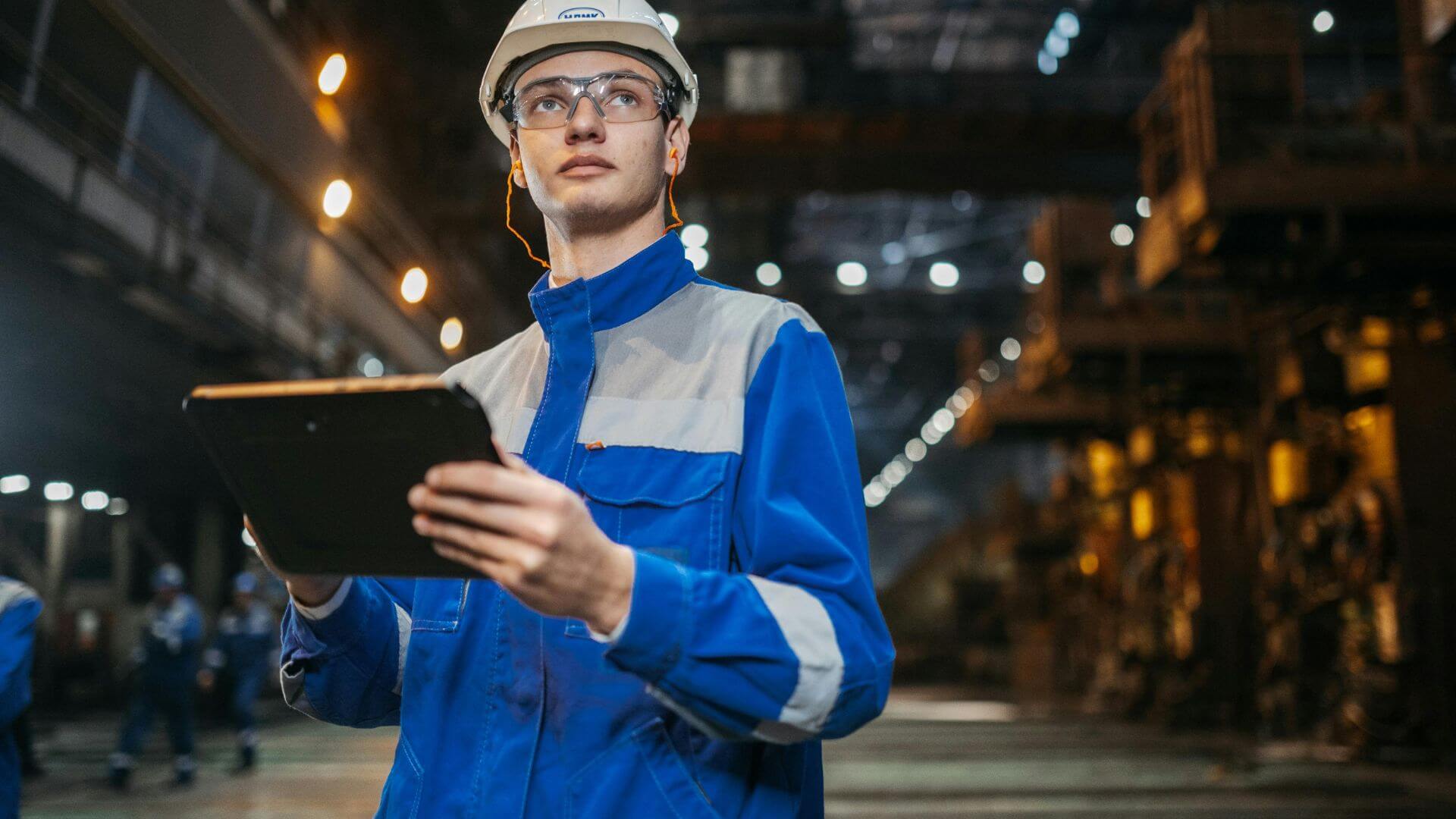Operario con casco, protección visual y tablet dentro de una planta, en una escena vinculada con la seguridad industrial.