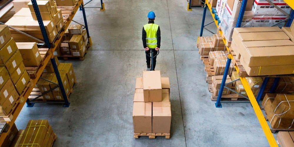 Trabajador de logística traslada un pallet con cajas entre las estanterías de un depósito.